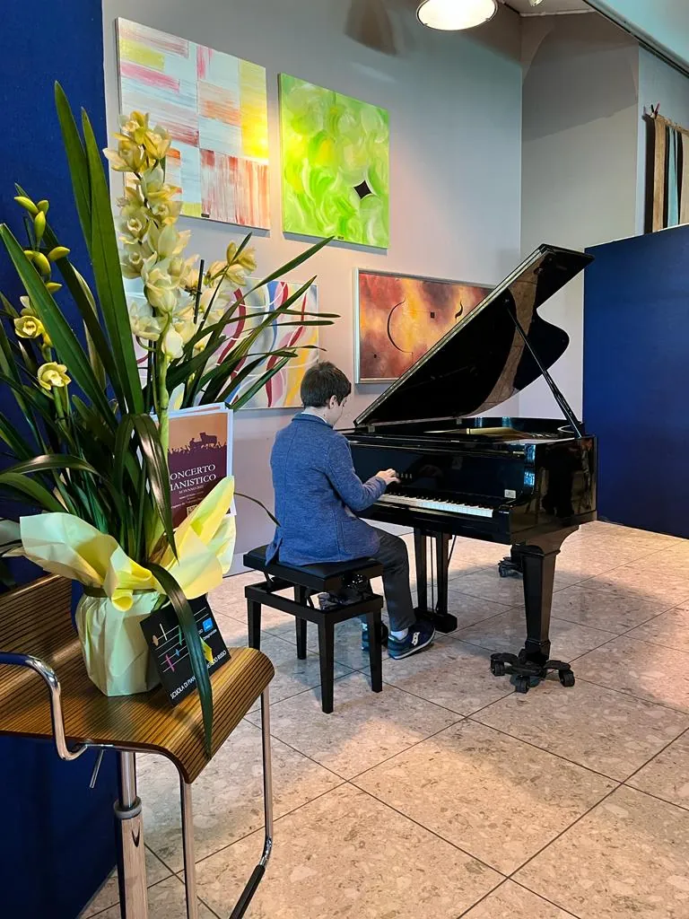 Un ragazzo suona al saggio, accanto a un mazzo di orchidee