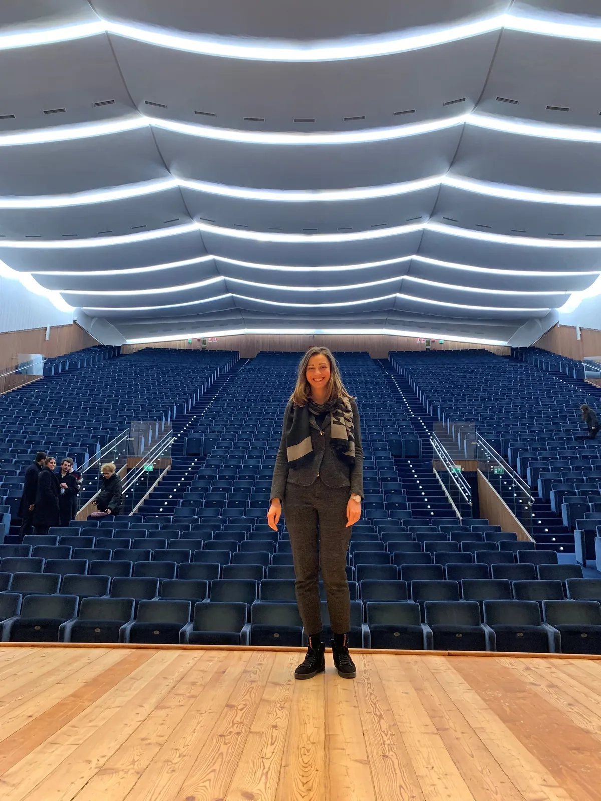 Valentina Dzhegnaradze in piedi sul palco di una grande sala da concerto, le poltrone blu alle spalle